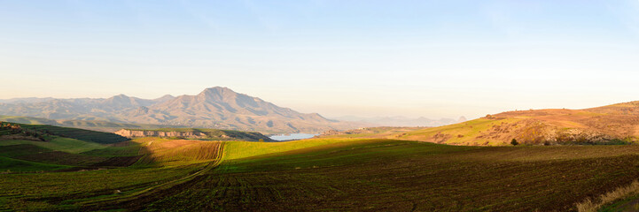 plowed fields look like alpine meadows in the light of the setting sun with mountain ranges and a lake on a clear sunny day.