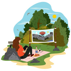 A young woman is relaxing in a park, drinking wine and watching a movie on the street. Street cinema