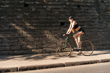 Image of pretty blonde woman riding bicycle through city street on summer sunny day