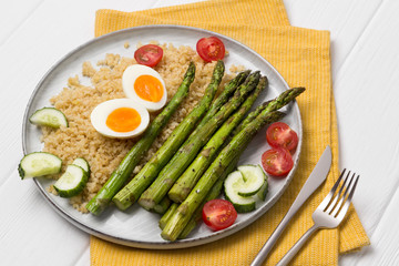 Baked green asparagus, bulgur, fresh tomatoes, cucumber and boiled eggs with herbs on a plate