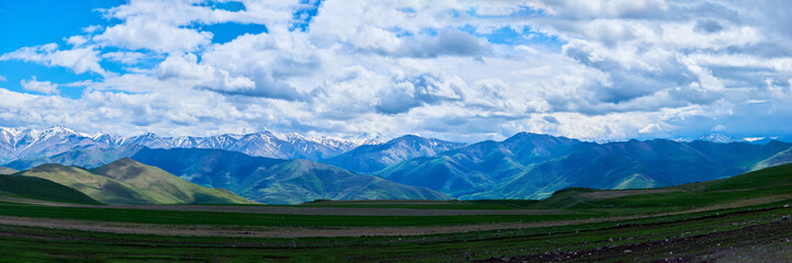 View of mountain snowy ridges on a bright sunny day with clouds in the sky.