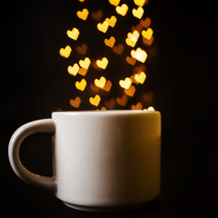 White mug on a dark background. In the background are heart-shaped lights. Cute festive creative still life. Place for text. The concept of Valentine's Day, love.