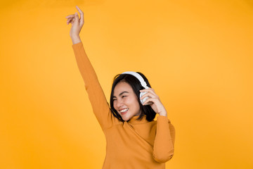 women dress in orange and wear white headphones. And dancing happily. Orange backdrop.