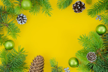 Christmas frame mockup. Pine cones, fir branches and Christmas balls on yellow background. New year flat lay, top view with copy space