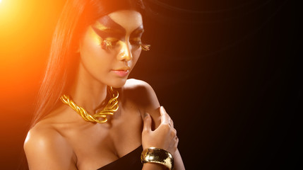 Fashion Young Asian Woman Tanned skin fancy eyelash black straight hair beautiful make up fashion decorate with Golden Foil or Gold leaf with bracelet and earrings. Studio Lighting dark Background