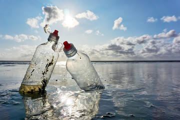 Plastic bottles with red bottle caps standing in the sea with blue sky and backlight at low tide. Concept of plastic pollution of the sea and marine life. Beat Plastic Pollution.       