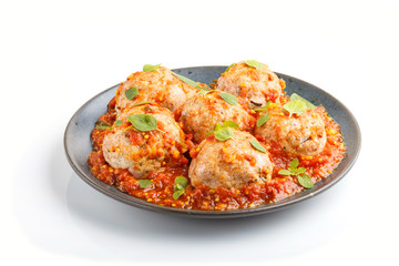 Pork meatballs with tomato sauce, oregano leaves, spices and herbs on blue ceramic plate isolated on white background. side view