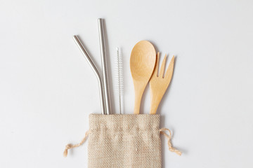 Flat lay of reusable stainless steel straw with wooden spoon in natural sack bag on white...