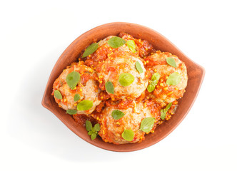Pork meatballs with tomato sauce, oregano leaves, spices and herbs in clay bowl isolated on white background. top view