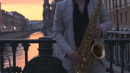 Saxophonist in a light suit on a bridge in the setting sun, plays the saxophone.