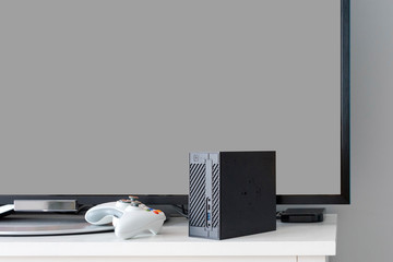 Flat LCD television on white cabinet in the living room with dark gray wall. Video gaming console and gamepad. Gamer station mockup