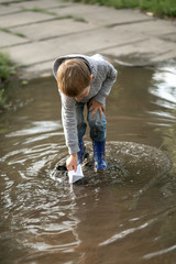 little boy launches a boat in a puddle