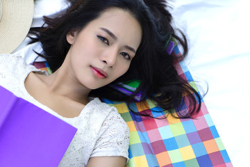 Young woman lying down with book looking up at camera.