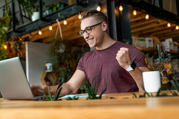 Cheerful young man in casual wear raise arm and looking happy while working at the desk in office