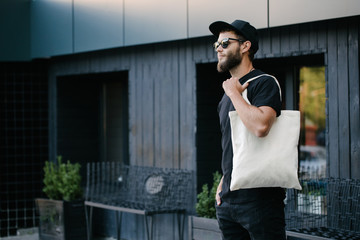 Young man holding white textile eco bag against urban city background. . Ecology or environment...