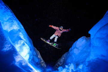 Active male snowboarder dressed in a white and pink sportswear jumping between the snow slopes