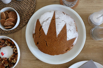 Homemade sponge cake served on a table with dishware, cookies, nuts and vase of flowers. Top view.