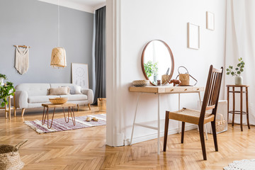Modern and design home interior of open space with wooden desk, coffee table, sofa, chair, plants, mirror, macrame and elegant accessories. Stylish and minimalistic home decor. Template. Bright rooms.