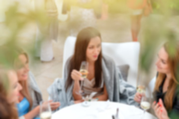 Blur portrait of smiling girls drinking wine in sunny day and talking around. Relaxed women drinking champagne in restaurant. Friends enjoying cocktails in speakeasy bar.Friendship and social concept