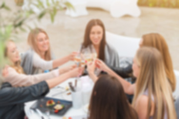 Blur portrait of smiling girls drinking wine in sunny day and talking around. Relaxed women drinking champagne in restaurant. Friends enjoying cocktails in speakeasy bar.Friendship and social concept
