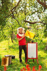 A beekeeper in a protective cap launches into work a honey extractor on the bee farm. Beekeeping