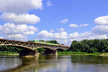 Fototapeta na wymiar The green and yellow train crossing the Srednicowy Bridge in Warsaw, Poland. It is a railway bridge over the Vistula River in Warsaw, north of the Poniatowski Bridge.