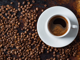 White espresso coffee Cup on vintage rusty background with scattered roasted coffee beans