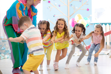 Preschool kids playing teamwork game together with clown