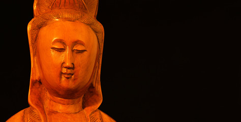 Buddhist religion and meditation. Kannon of Guanyin, the Goddess of Mercy, wooden statuette on black background (with copy space)