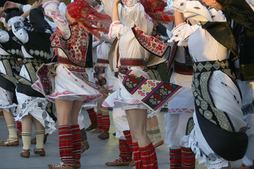 Professional dancers of the Timisul Folklore Ensemble hold hands in a traditional Romanian dance wearing traditional beautiful costumes.