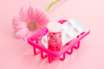 Women's health, medicine and healthcare concept. Pink tablets and glass bottle in the basket on a flower background. Close up