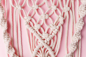 A handmade 100% cotton macrame wall decoration hanging on pink wall. Decoration for the interior. Trendy handcrafted decor for house
