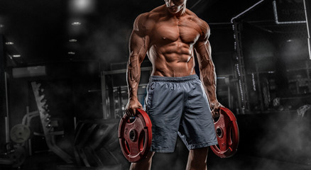 Young male athlete bodybuilder posing and doing sports exercises in the gym