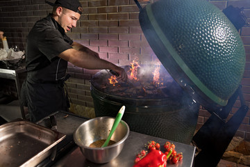 Food concept. Young chef in uniform holds hands on a grill stove. Flames erupt from under on...