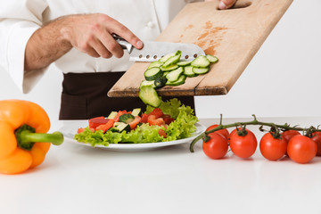 Cropped image of young cook man in uniform cutting vegetable salad on wooden board