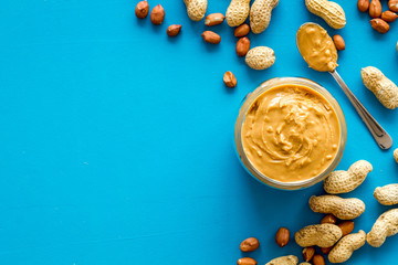 Make peanut butter with paste in glass bowl on blue background top view copyspace