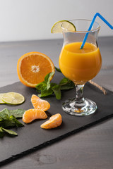 Orange juice in a glass with tube on a black board on a light background. Near orange, mint, tangerine slices. Healthy food