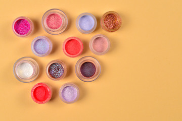 Obraz na płótnie Canvas Cosmetics. Makeup. Jars with crumbly bright shadows, glitter. Pink,peach, golden colors on beige background. Closeup. Space for text or design.