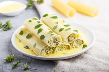 Cannelloni pasta with egg sauce, cream cheese and oregano leaves on a gray concrete background with linen textile. side view, close up.