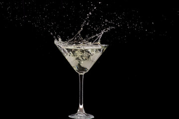 glass of martini and splash from falling ice on a black background