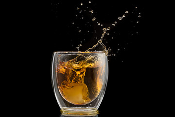 glass with whiskey and falling ice, double wall, splashes and drops