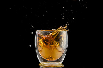 glass with whiskey and falling ice, double wall, splashes and drops