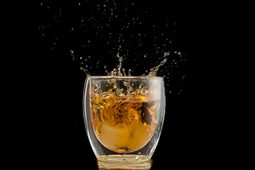 glass with whiskey and falling ice, double wall, splashes and drops