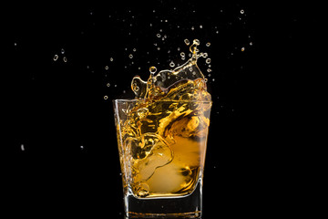 glass with whiskey and falling ice, splashes and drops