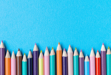 Border of colored pencils against a bright blue textured background. Back to school concept with copy space