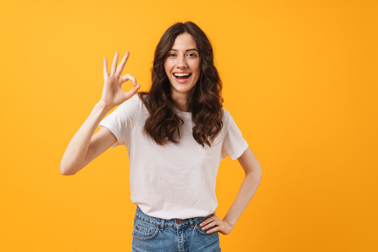 Image of amazed brunette woman wearing casual clothes smiling and showing ok sign at camera