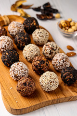 Healthy energy balls of nuts, oatmeals and dried fruit with coconut, flax and sesame seeds on wooden board on a white background, vertical orientation, top view