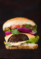 Fresh organic beef burger with cheese  and sauce with vegetables on wooden board. Macro
