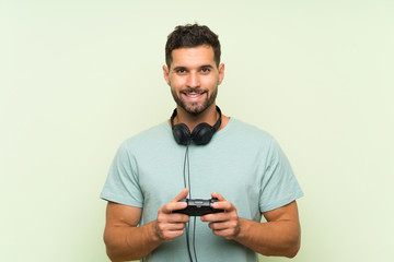 Young handsome man playing with a video game controller over isolated green wall smiling a lot © luismolinero
