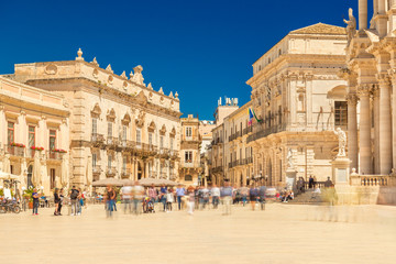 View of The Central Square in Ortygia (Ortigia, Piazza Duomo) with walking people. Historical buildings in the famous Sicilian town Syracuse (Siracusa), Italy - obrazy, fototapety, plakaty